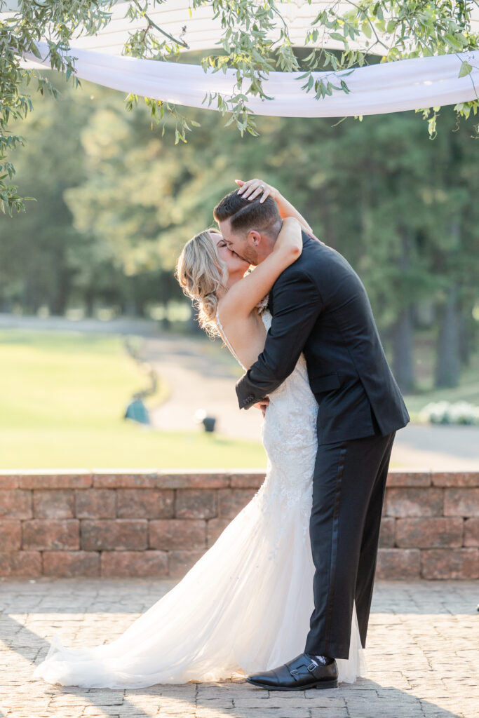 Bride and groom aisle first kiss during outdoor wedding ceremony