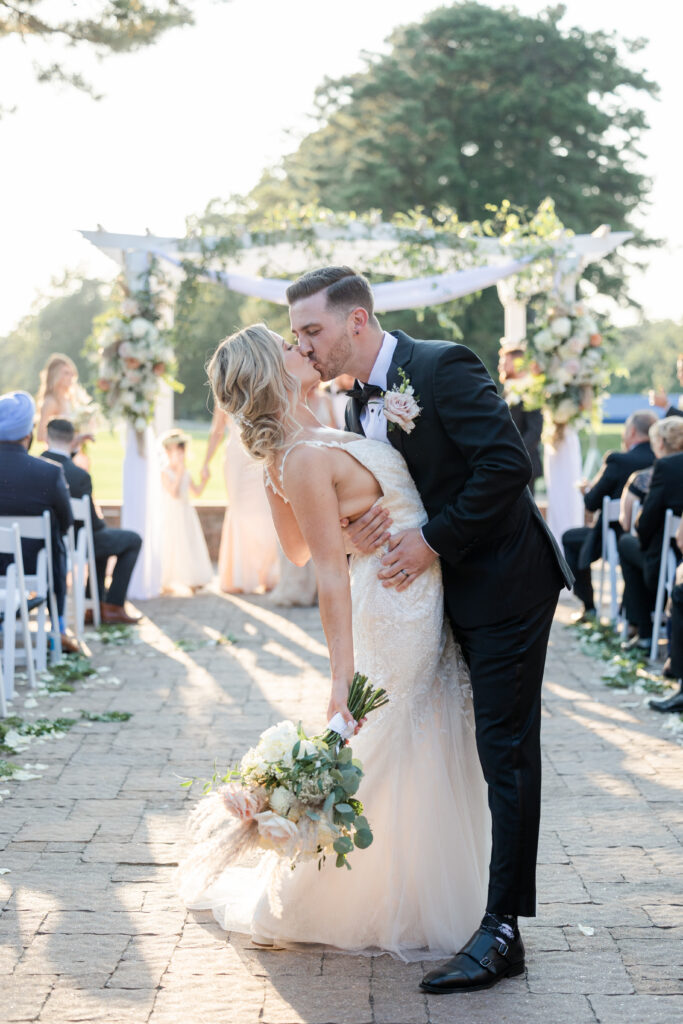 Bride and groom aisle kiss during outdoor wedding ceremony