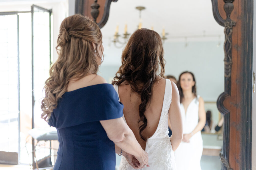 Bride getting dressed with mom in front of classy mirror