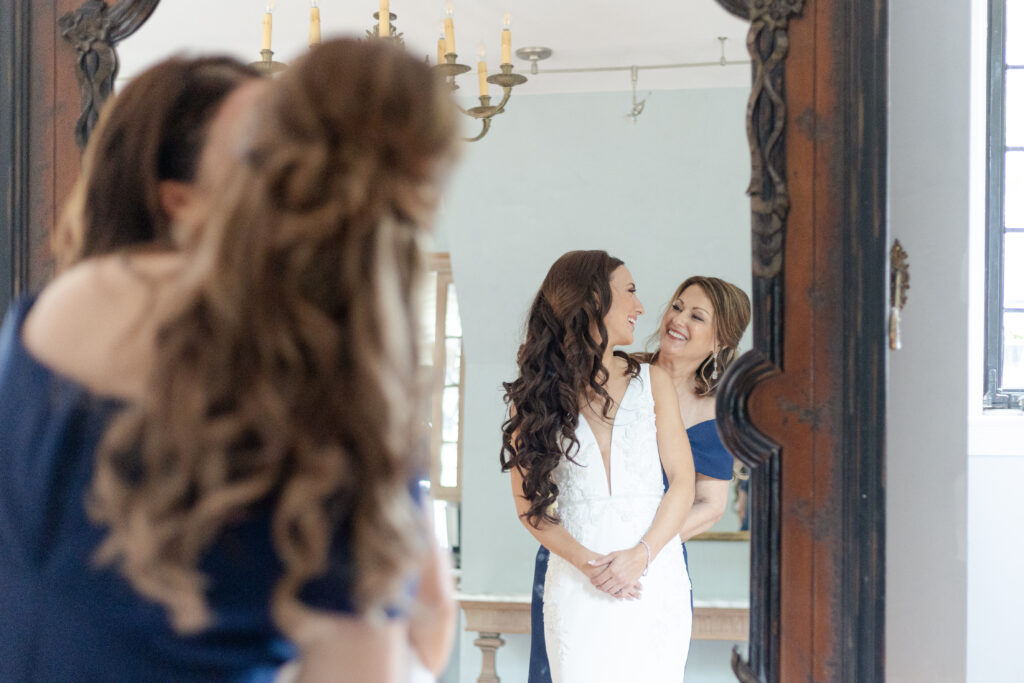 Bride getting dressed with mom in front of classy mirror