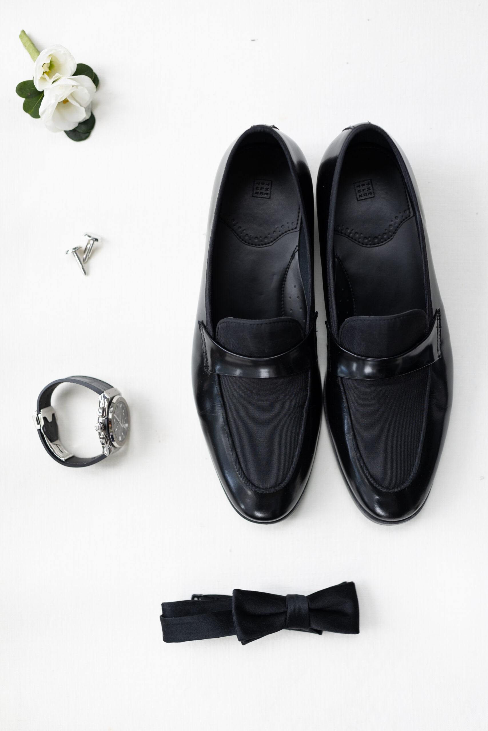 Groom flatlay details with shoes, watch, cufflinks, bowtie, and boutonniere