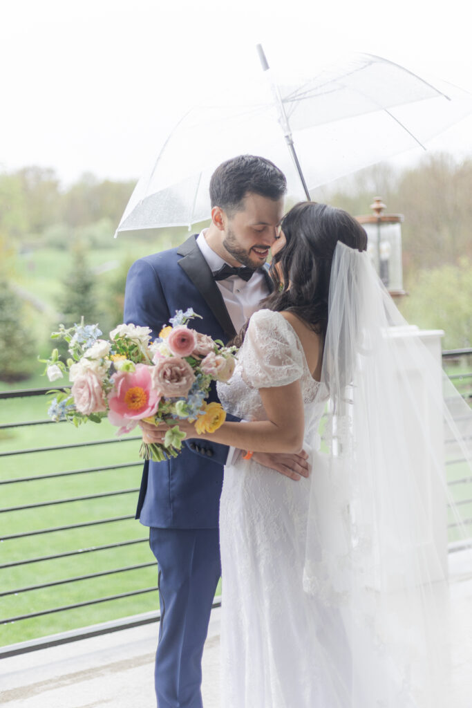 Bride and groom outside wedding venue under clear umbrella