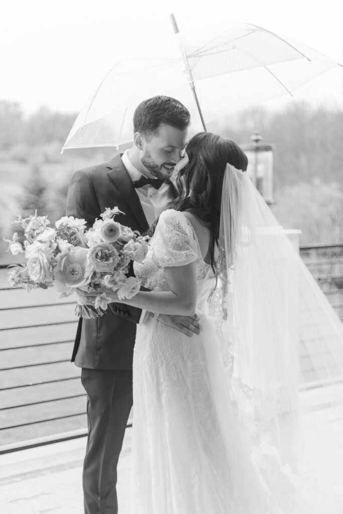 Black and white of bride and groom outside wedding venue under clear umbrella