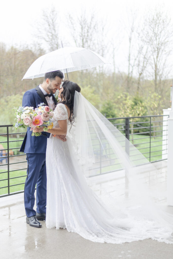 Bride and groom outside wedding venue under clear umbrella