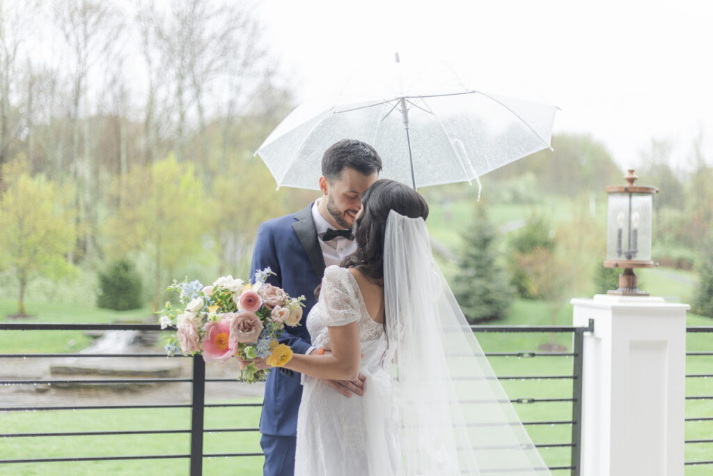 Bride and groom outside wedding venue under clear umbrella