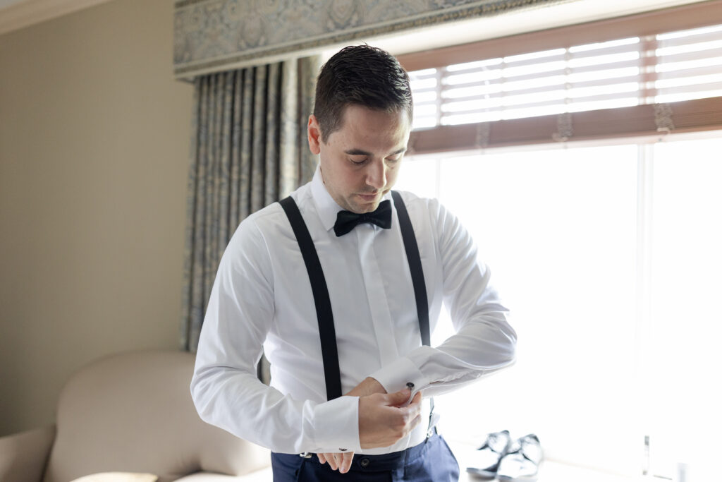 Groom putting cufflinks on inside groom's suite at Madison Hotel