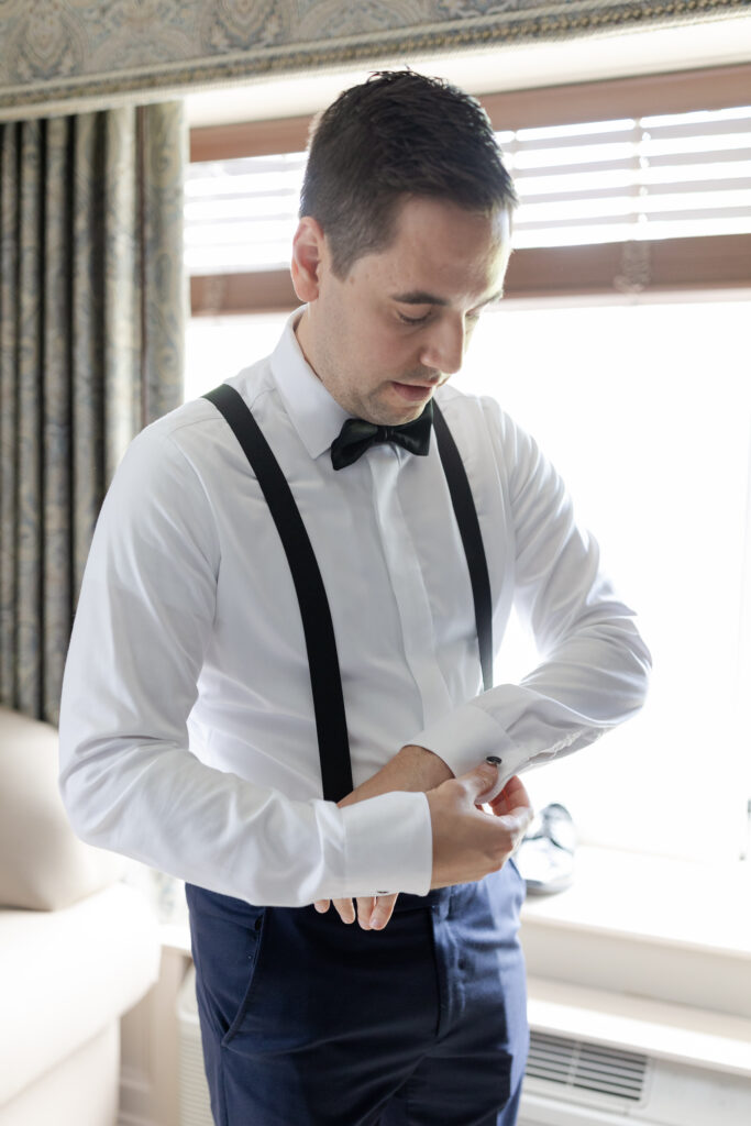 Groom putting cufflinks on inside groom's suite at Madison Hotel