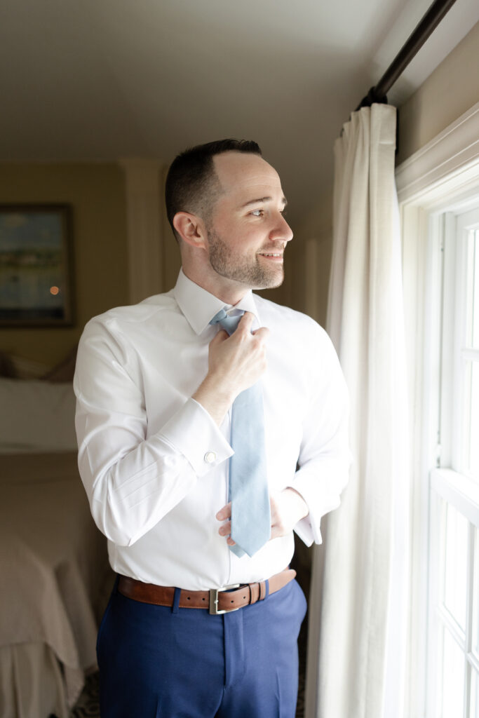 Groom putting on tie inside Olde Mill Inn suite