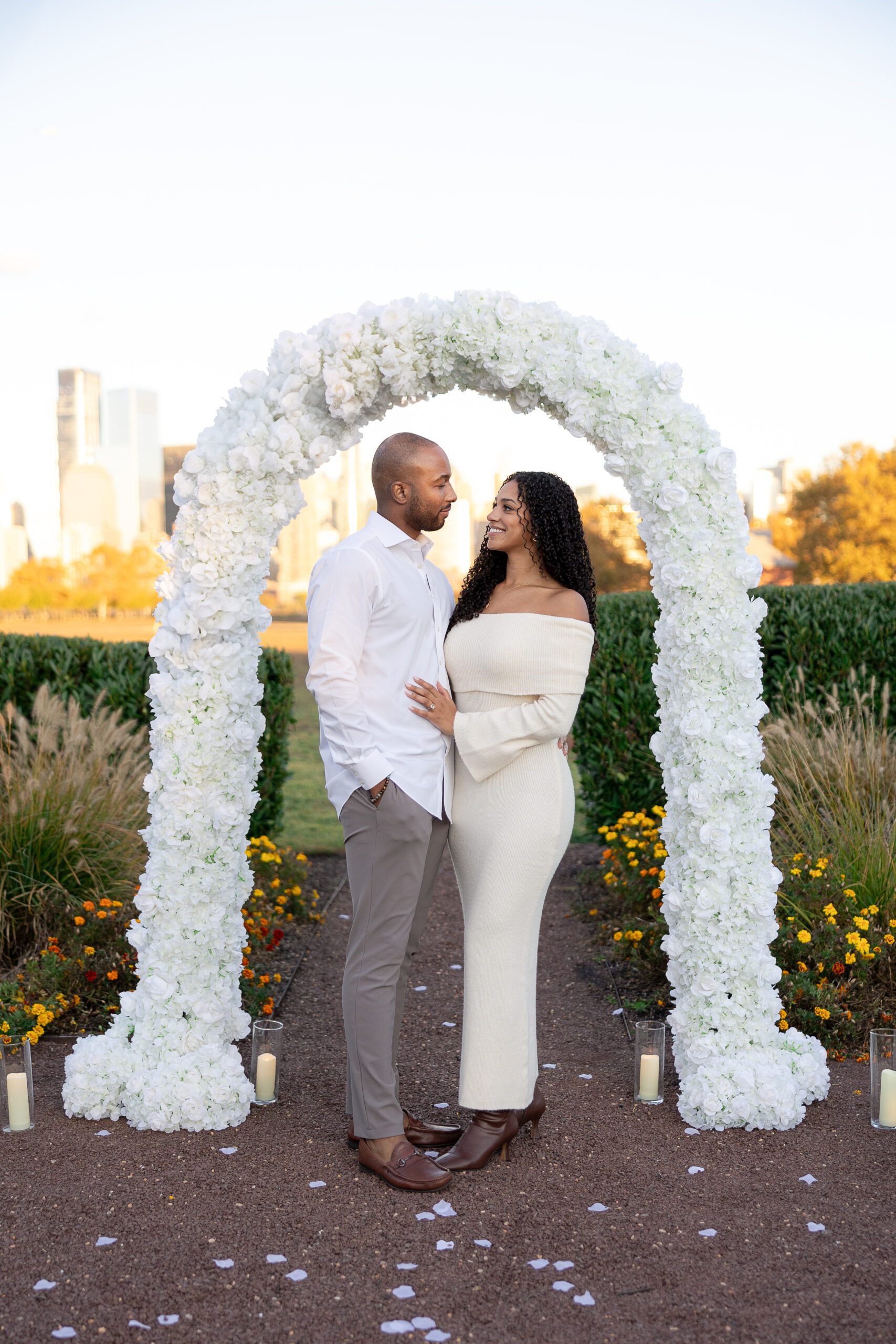 Engagement photos at Liberty State Park with Manhattan skyline and white floral arch in the background